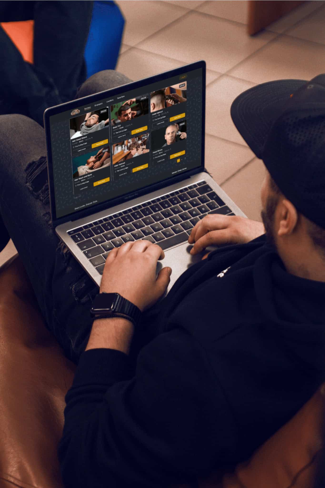 A person wearing a black cap and smartwatch is sitting and using a laptop, browsing a website with multiple profile cards displayed on the screen.